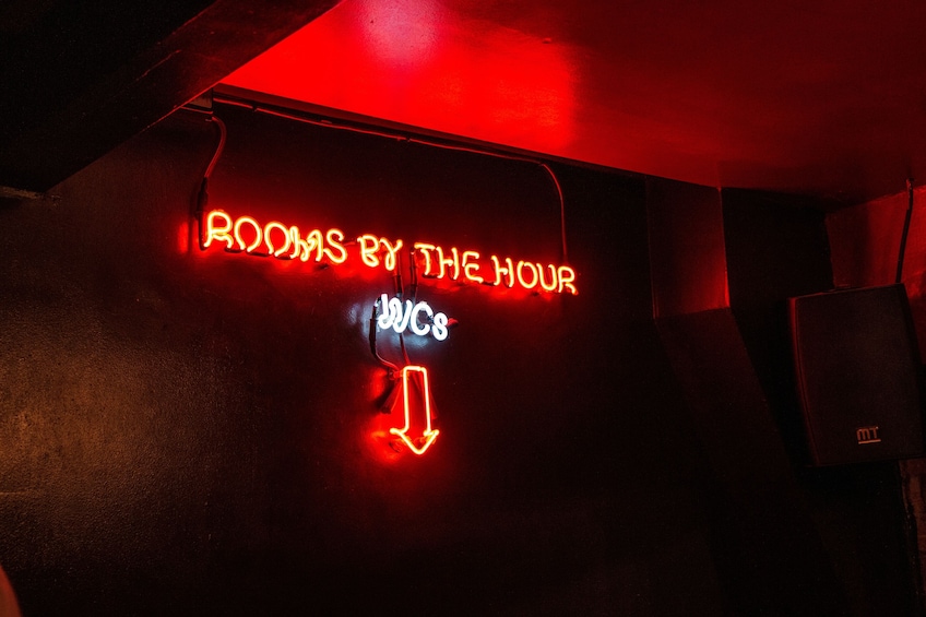 A neon sign with the text 'ROOMS BY THE HOUR' and an arrow pointing downwards. 2