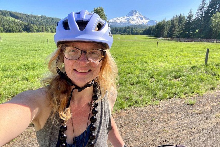 A person wearing a helmet and a necklace, standing in a grassy field with a mountain in the background. 2