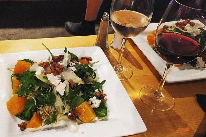 A white plate with a salad, two wine glasses, and a salt shaker on a wooden table. 5