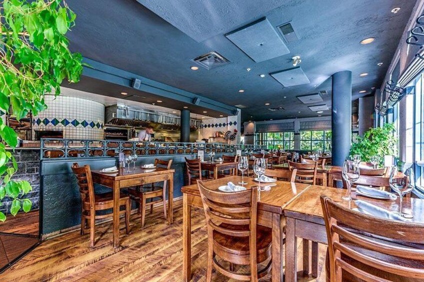 A restaurant interior with wooden tables, chairs, and a kitchen in the background. 1