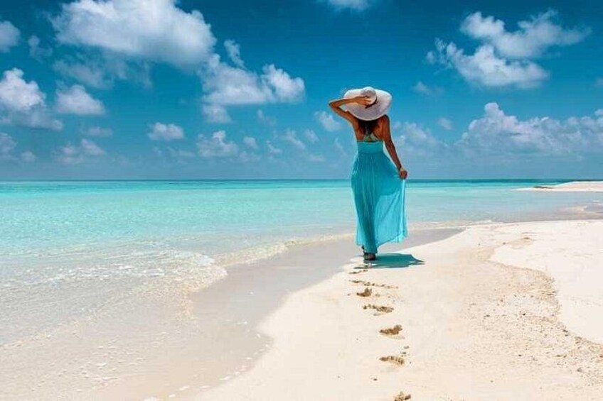 A person walking on a sandy beach with clear blue water and a clear sky. 1