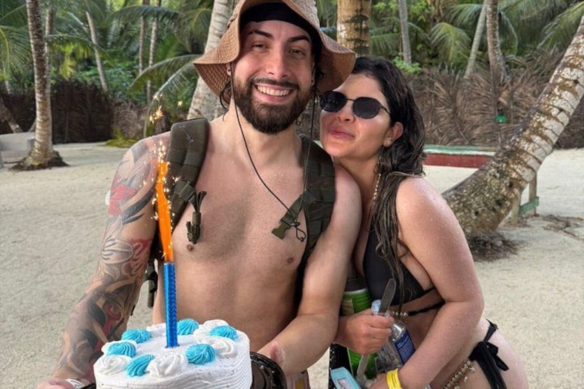 A person with a backpack and tattoos holding a cake with blue frosting and a blue candle. 2