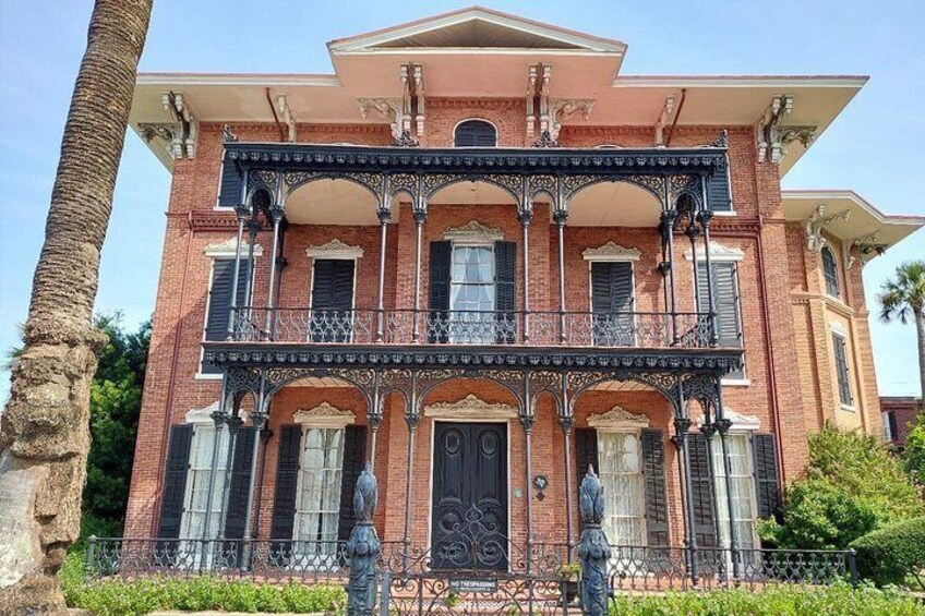 A large brick building with a balcony, ornate railings, and a statue in front. 4