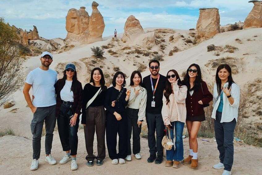 A group of people standing on a sandy terrain with rock formations in the background. 1