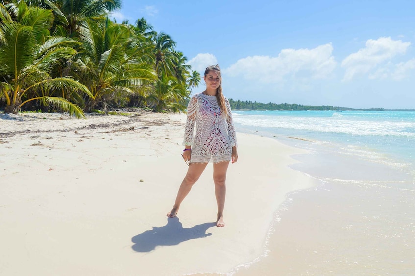 A person standing on a sandy beach with palm trees and ocean waves in the background. 1