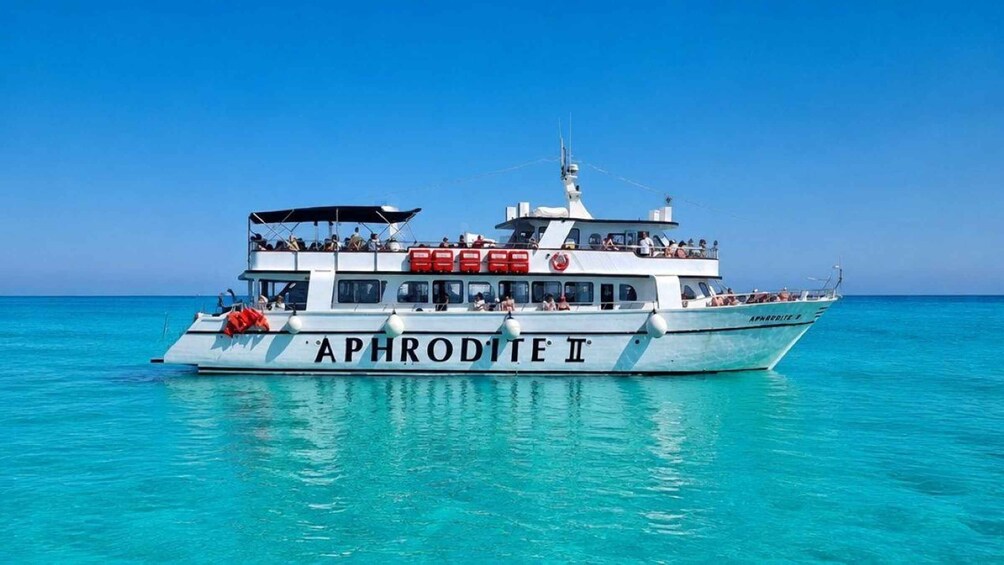 A white boat named 'APHRODITE II' with passengers on deck, floating on turquoise water. 2