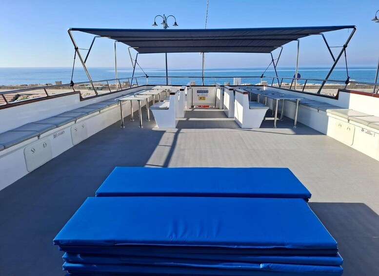 A boat deck with a covered seating area, tables, and a blue mat in the foreground. 3