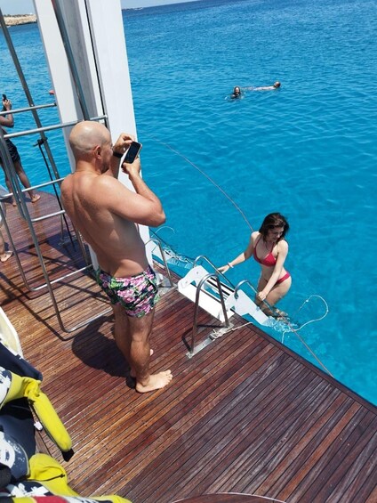 A man taking a photo of a woman in a bikini on a boat deck. 4