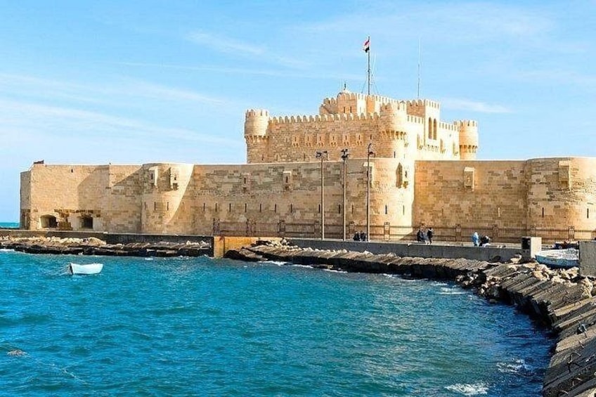 A coastal fortress with a flag, a small boat, and a clear blue sky. 1