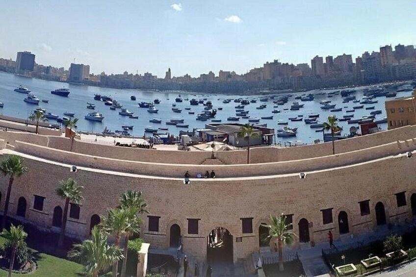 A coastal cityscape with a large port filled with boats, a sandy beach, and a historic stone wall. 4