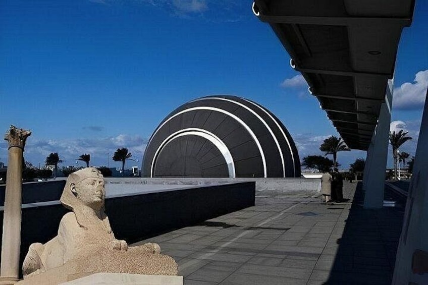 A modern building with a curved facade, a large statue of a pharaoh, and a clear blue sky. 5