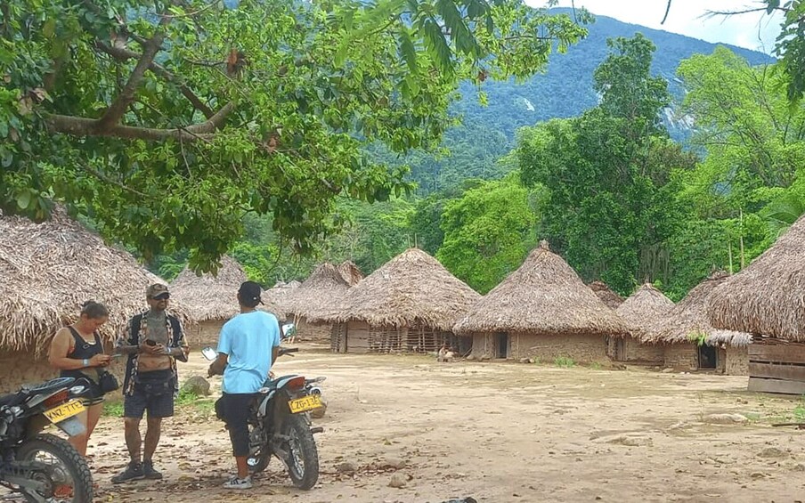 A rural village with thatched-roof huts, a dirt ground, and a mountain in the background. 5