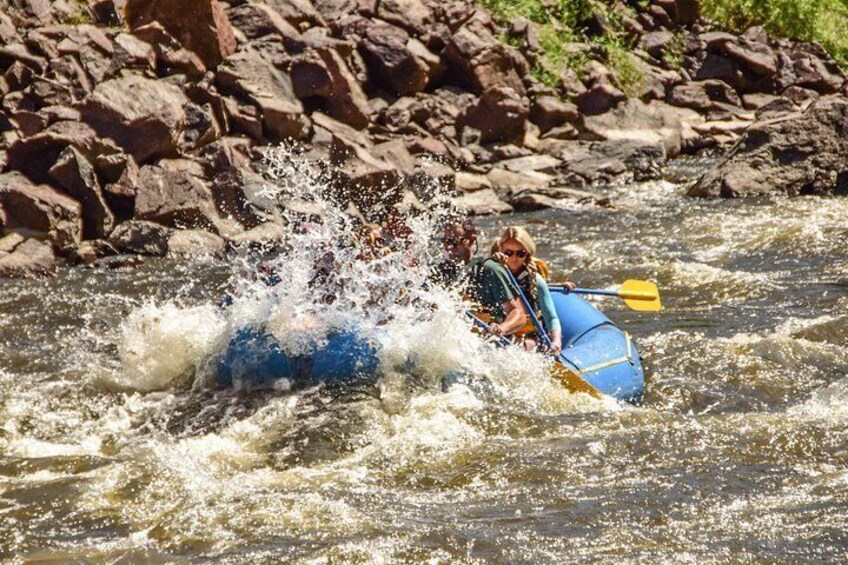 A person in a blue kayak navigating a river with a rocky riverbank. 5