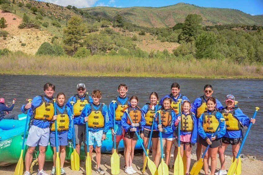 A group of people in blue jackets and yellow life vests standing by a river. 2