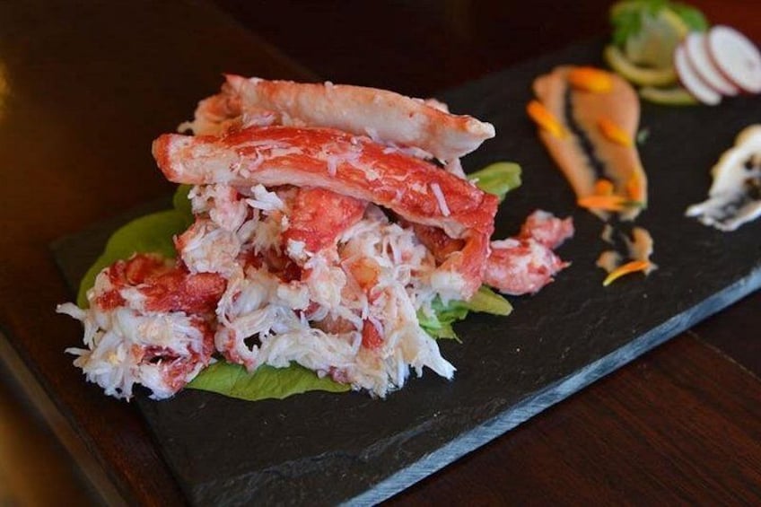 A crab dish on a black slate plate with lettuce and a side of sliced vegetables. 4