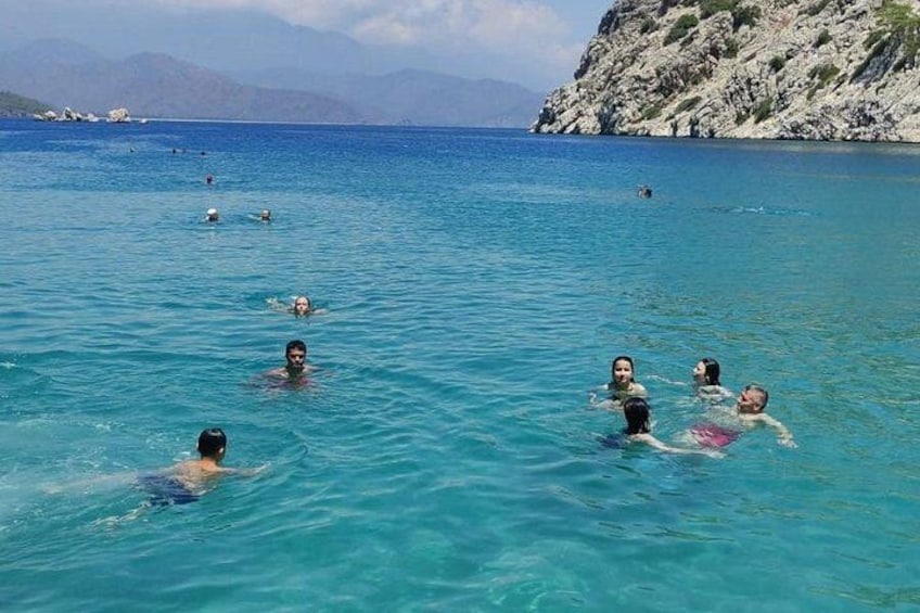 People swimming in a clear blue sea with rocky cliffs in the background. 3