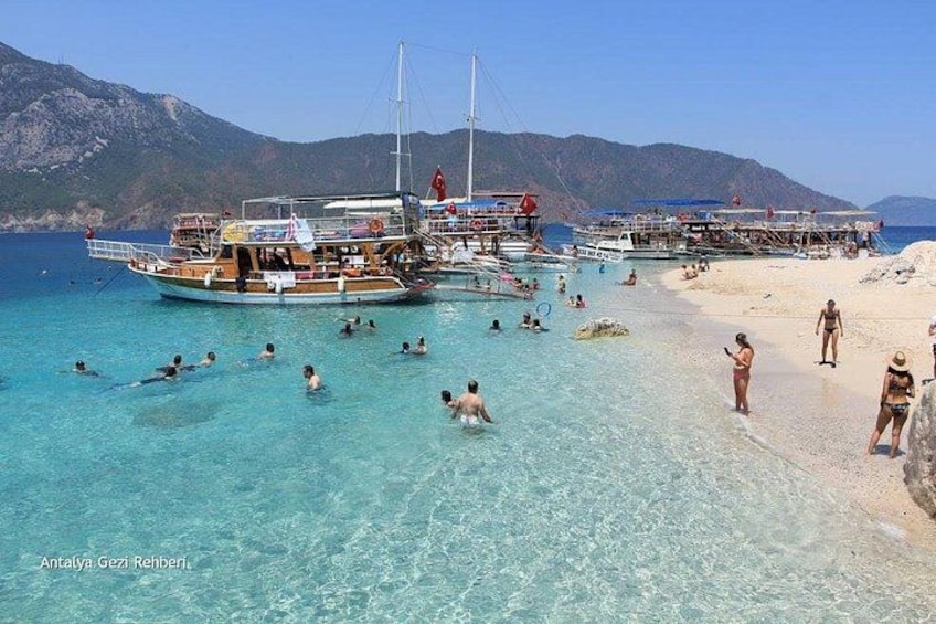 A beach with clear turquoise water, people swimming and sunbathing, and boats anchored nearby. 5