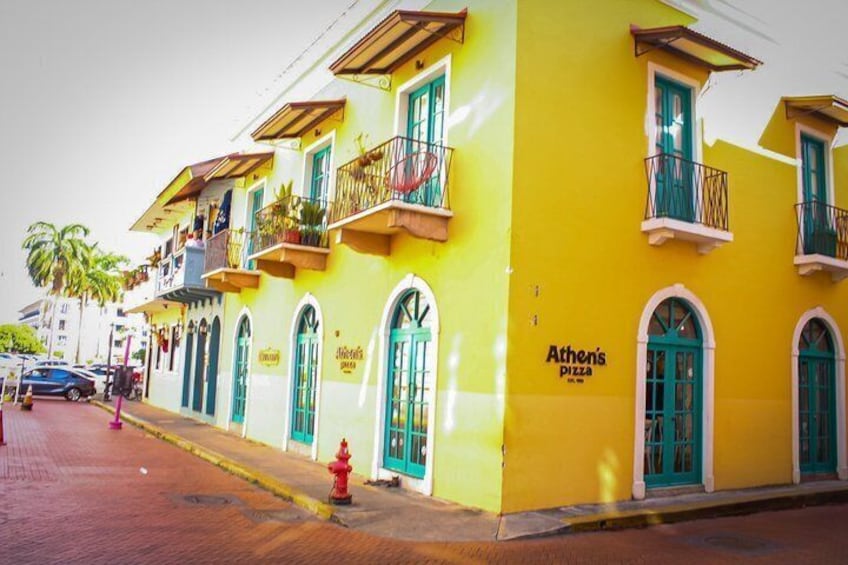 Un edificio giallo con balconi e un cartello con scritto 'Athen's Pizza'. 5