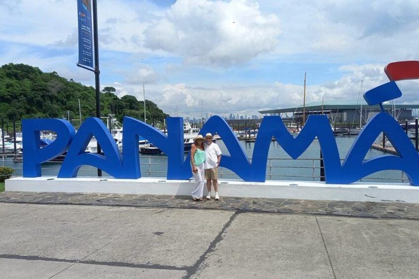 A large blue sign with the word 'PANAMA' and a waterfront with boats and a cityscape in the background. 1