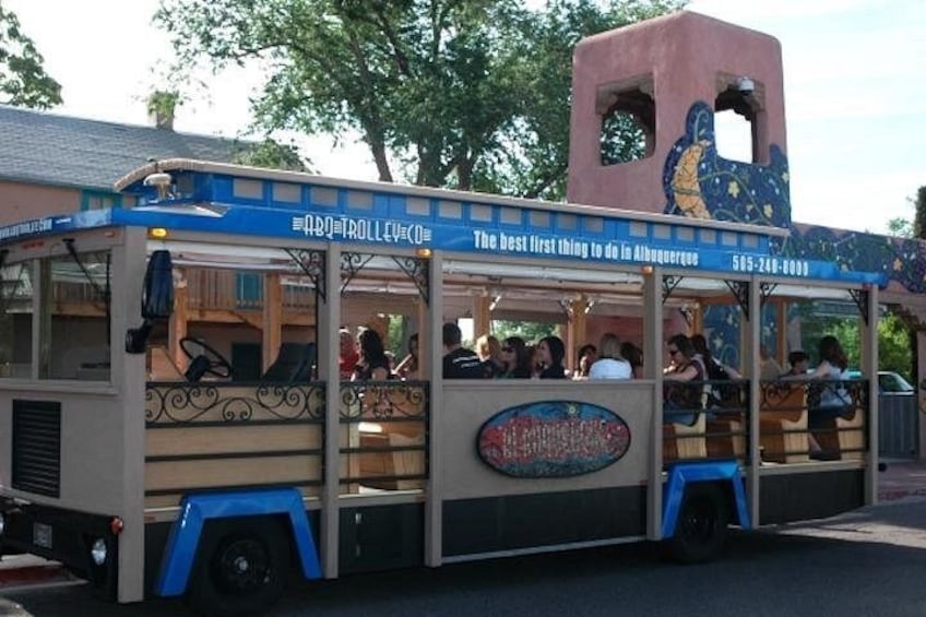 A trolley with passengers, a blue awning, and a building with a clock tower. 1