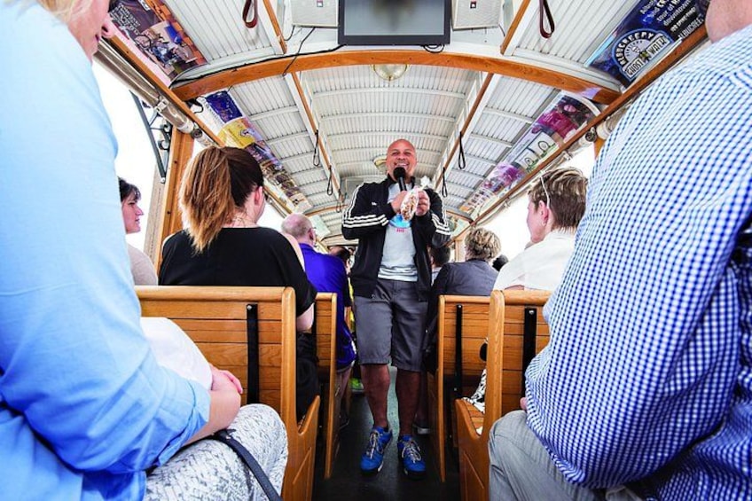 A boat interior with wooden benches, a person standing at the front, and passengers seated. 3