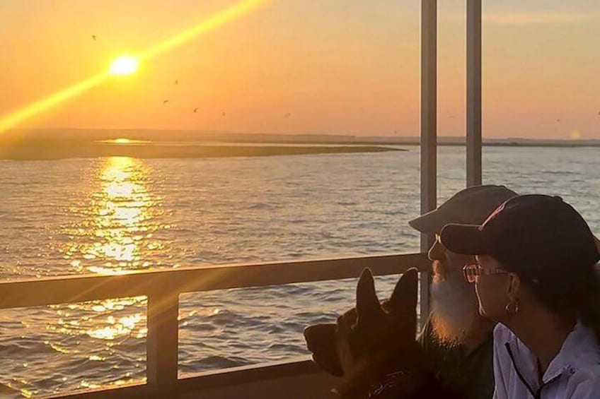 A sunset over water with a person holding a phone. 2