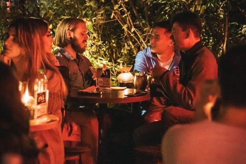 Un groupe de personnes est assis autour d’une table, avec des boissons et une bougie, dans un endroit extérieur à la lumière tamisée. 3