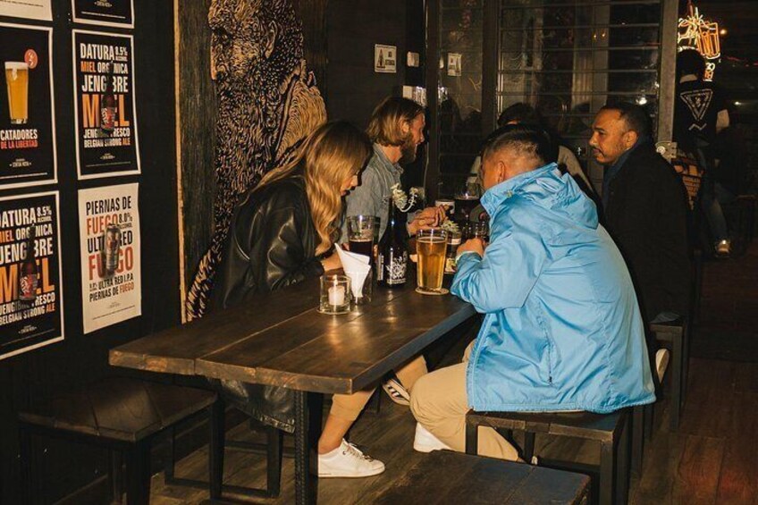 Un bar avec des clients assis à des tables, des meubles en bois et des affiches aux murs. 2