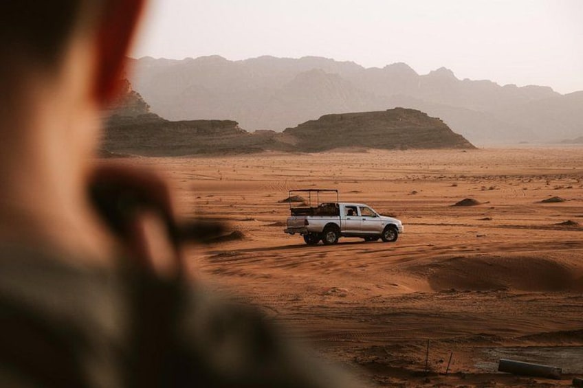 A desert landscape with a white pickup truck parked on the sand. 1