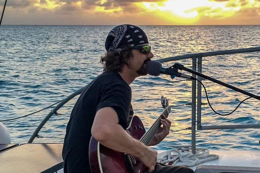 A person playing a guitar on a boat with the ocean in the background. 1