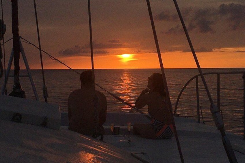 Two people sitting on a boat deck, facing the sunset over the ocean. 5
