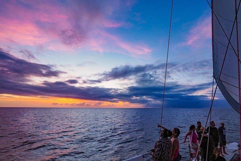 A sunset over the ocean with a sailboat and people on deck. 4