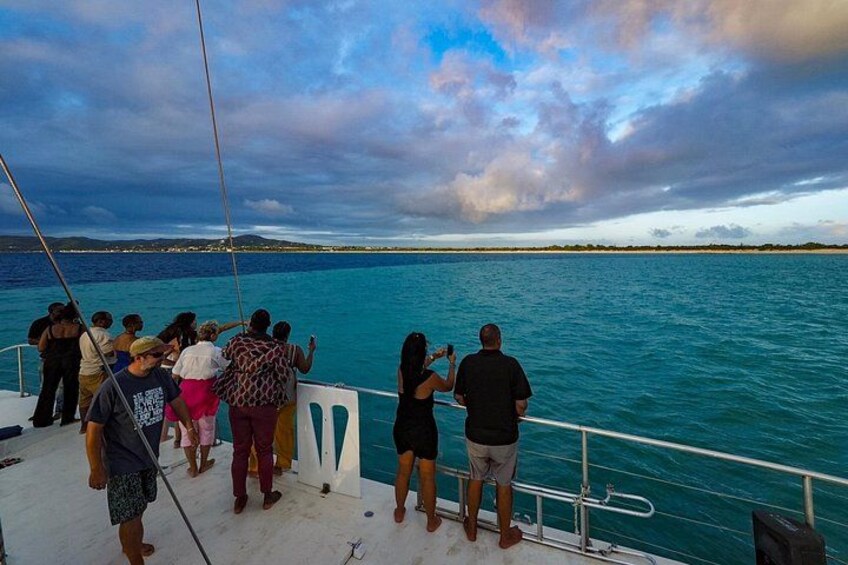 A group of people on a boat, looking out at a calm sea with a distant shoreline. 2