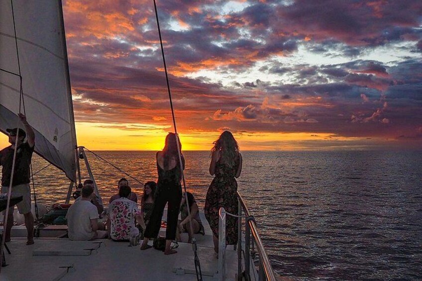 A sunset on the ocean with people on a sailboat. 3