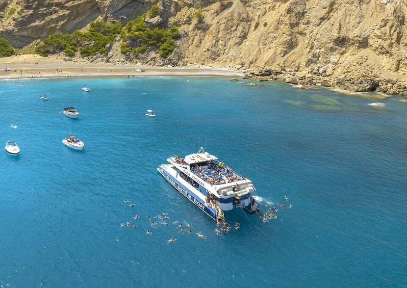 Un barco grande con pasajeros cerca de una costa rocosa y varios barcos más pequeños en el agua. 1