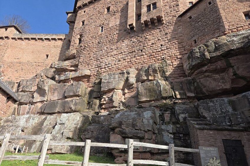 A historic stone castle with a large, fortified wall and a wooden fence in the foreground. 4