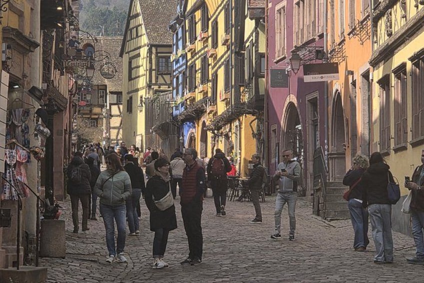 A cobblestone street in a European town with colorful buildings and people walking. 4