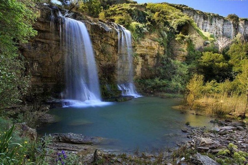 Una cascada se precipita en una piscina tranquila rodeada de vegetación exuberante y acantilados rocosos. 2