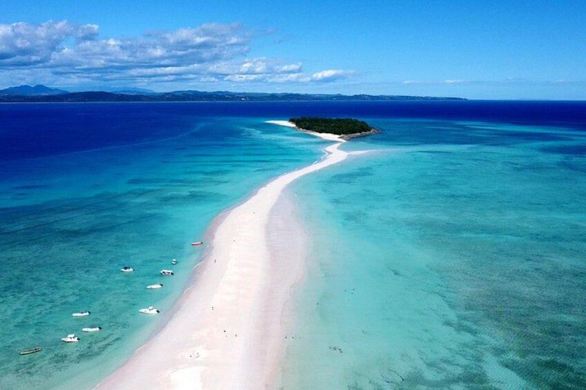 A beach with clear turquoise waters, a sandy shore, and a small island in the distance. 3