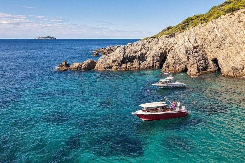 A red boat anchored near rocky cliffs, clear turquoise water, and a distant island. 5