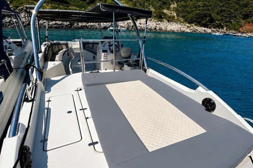 A boat's deck with a white cushioned area, metal railings, and a rocky shoreline in the background. 3