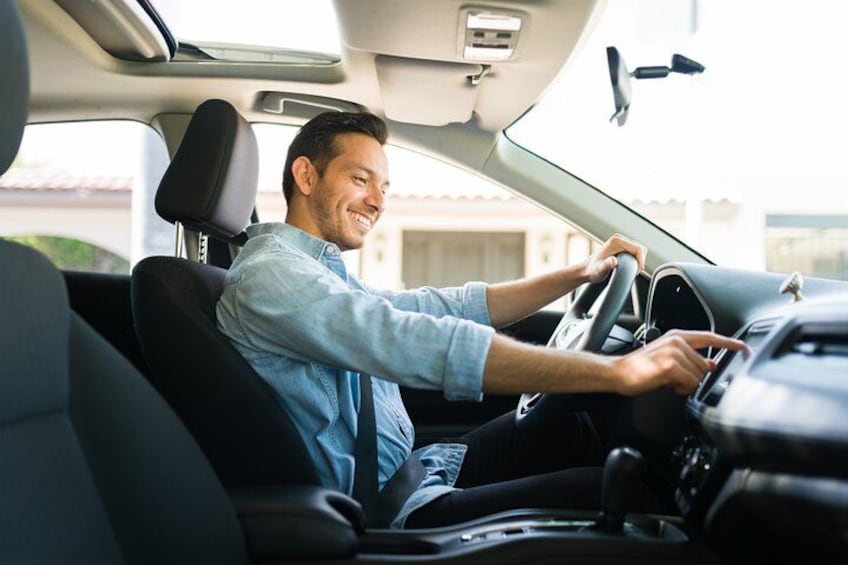 A person driving a car with a steering wheel, dashboard, and black seats. 2