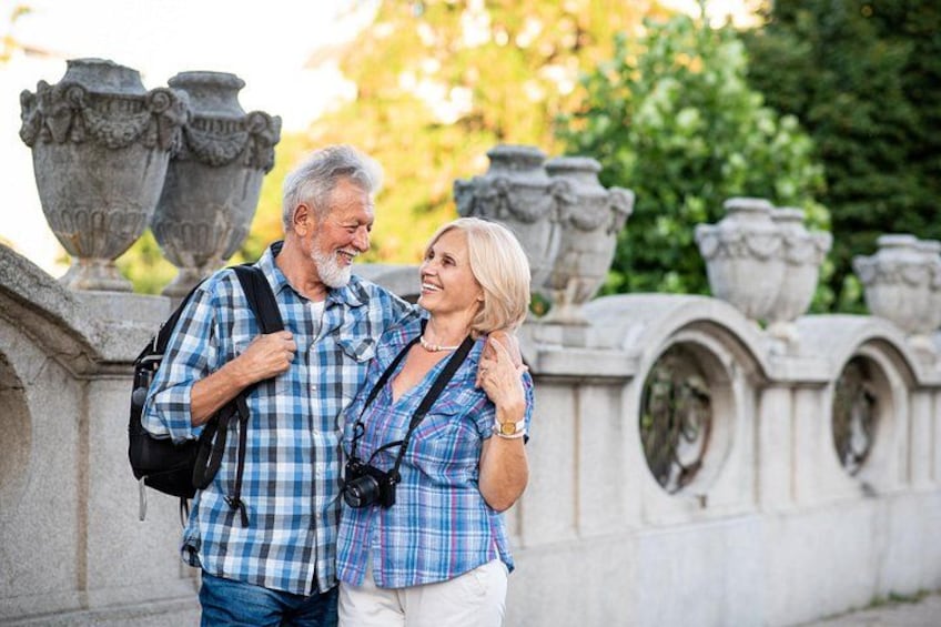 Two people standing in front of a stone wall with decorative urns. 3