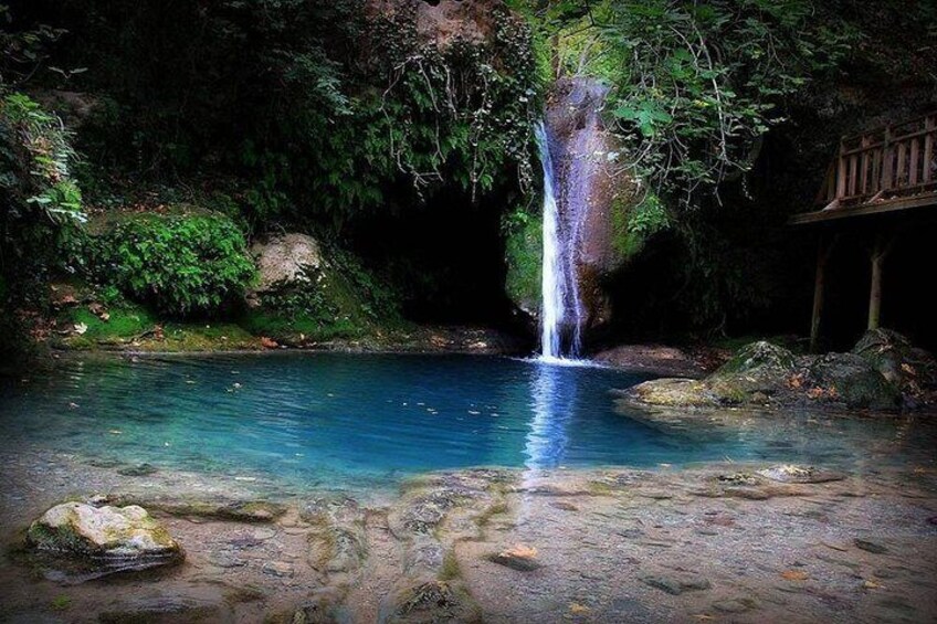 A waterfall, clear blue water, rocks, and greenery. 2