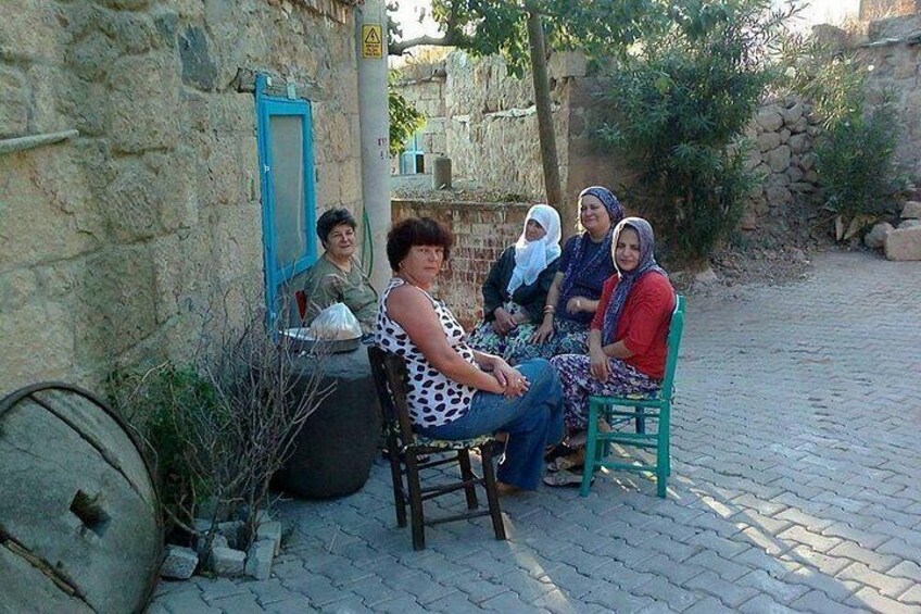 A group of women sitting on chairs outdoors, with stone walls and a cobblestone path in the background. 3