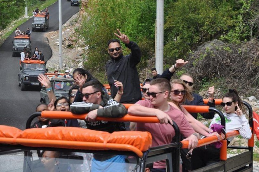 A group of people on a vehicle with orange railings, driving on a road with other vehicles. 2