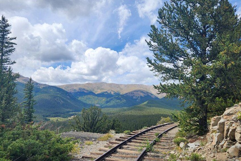A railway track winding through a mountainous landscape with pine trees and rocky terrain. 1