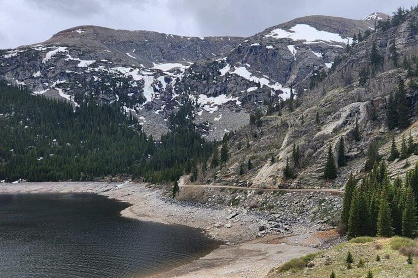 A mountainous landscape with a lake, a dirt path, and snow-capped peaks. 3