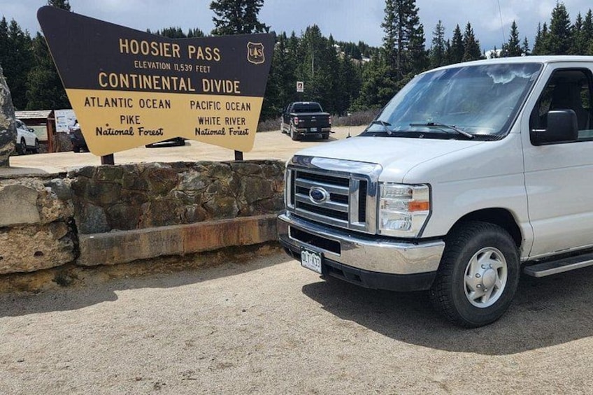 A white truck parked near a sign indicating the Hoosier Pass elevation and continental divide, with references to the Atlantic and Pacific Oceans and the White River National Forest. 5