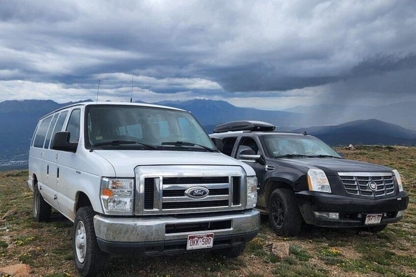 Two vehicles parked on a grassy field with mountains in the background. 2
